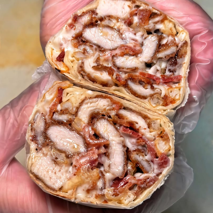 A Plainview Bagel Cafe chicken and bacon wrap, cut in half, revealing creamy sauce and fillings.