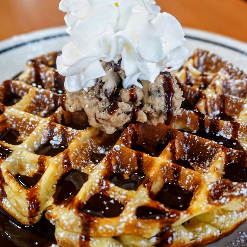 A waffle topped with chocolate syrup, powdered sugar, ice cream, and whipped cream.