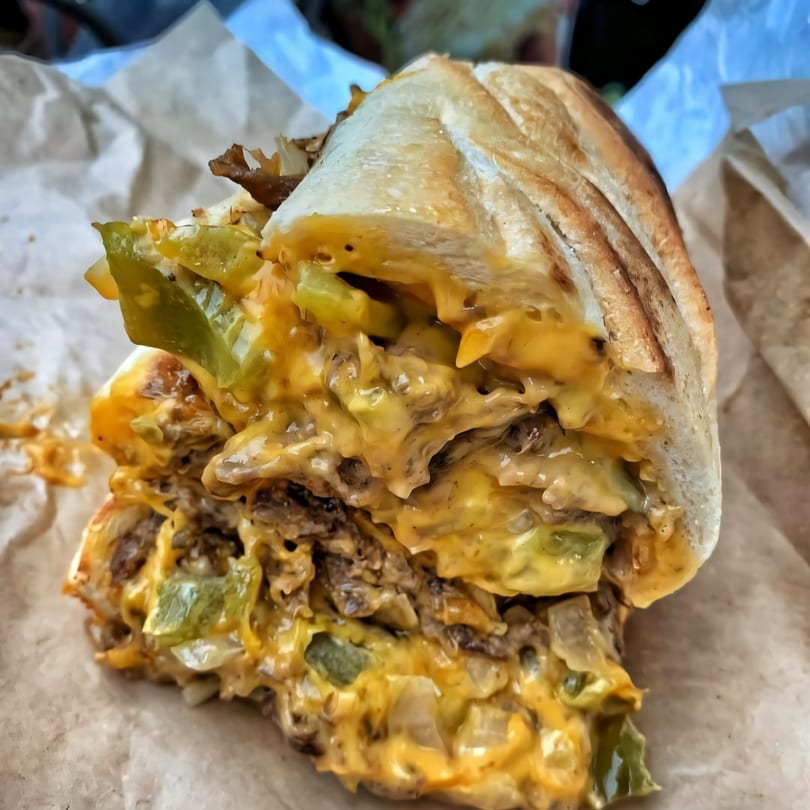 A Plainview Bagel Cafe cheesesteak sandwich, overflowing with melted cheese, green peppers, and steak.