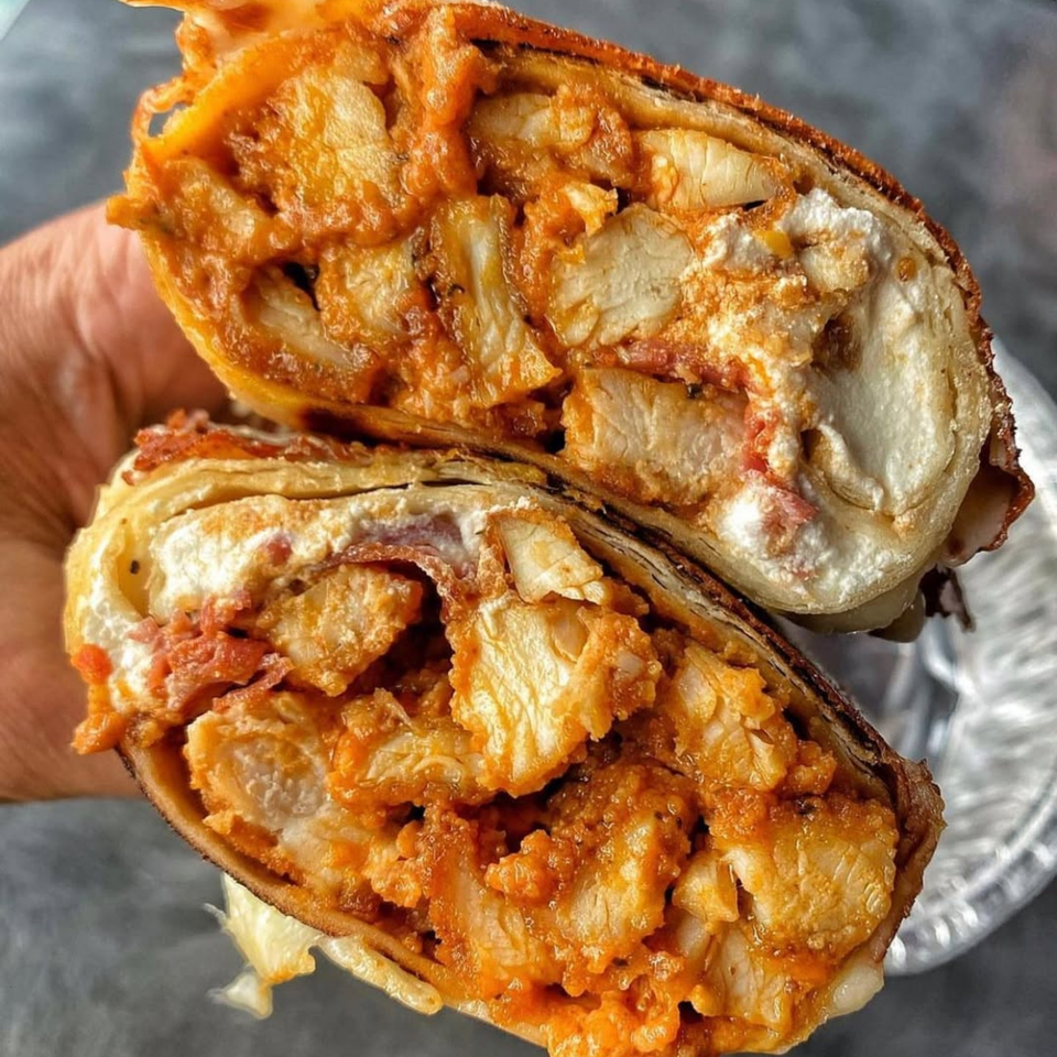 A Plainview Bagel Cafe buffalo chicken wrap, cut in half, revealing chicken, sauce, and cream cheese.